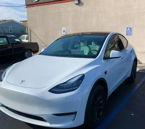 A white Tesla Model Y just after a full tint job with the A1 Auto Glass shop exterior visible behind it