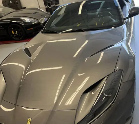 The hood of a Ferrari 812 in the bright A1 Auto Glass bay alongside other covered exotic cars