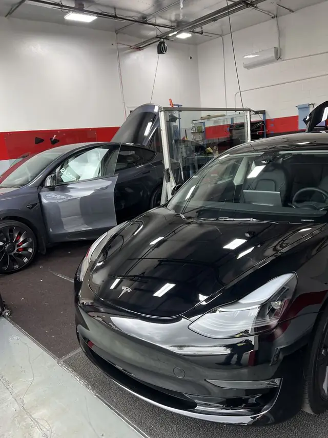 Two Teslas in the A1 Auto Glass bay being tinted, film tools racked along the wall