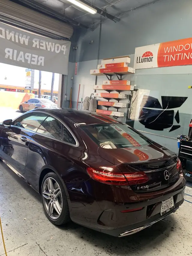 Llumar window film boxes stacked in the tint bay beside a freshly tinted Mercedes